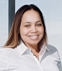 a smiling woman in a white shirt standing in front of a window